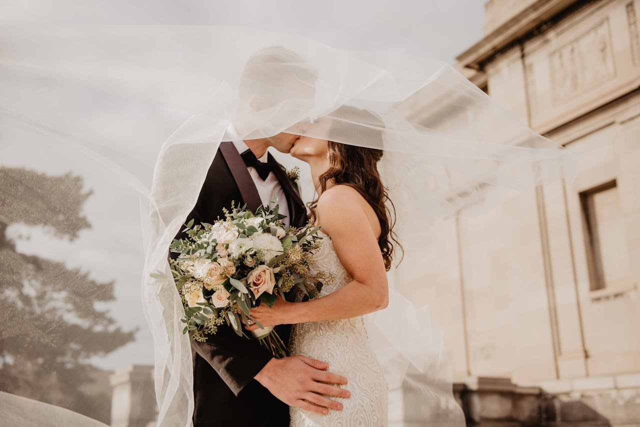 hero-img Bride and groom share a tender kiss under a veil, showcasing love and romance on their special day.
