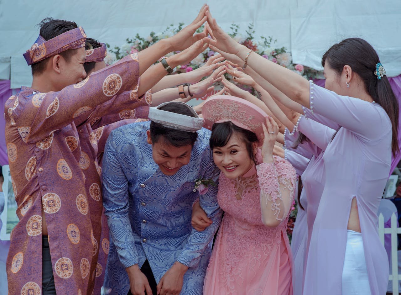about-me-01 Happy Vietnamese couple celebrates their wedding with friends in traditional attire outdoors.